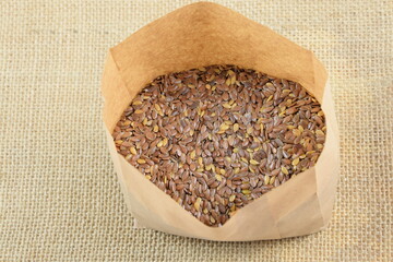 Flax seeds in paper bag, gluten free healthy grains, on jute fabric background