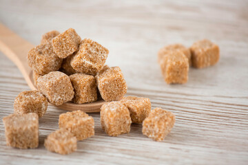 Brown sugar in a square cup and wooden spoon on a wooden table, healthy sugar is used for cooking food or desserts.