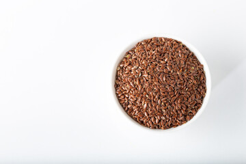 Flax seeds in white bowl on white background.