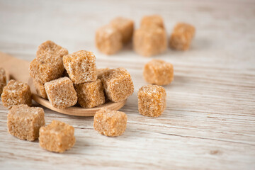 Brown sugar in a square cup and wooden spoon on a wooden table, healthy sugar is used for cooking food or desserts.