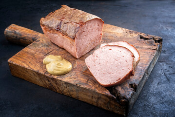Traditional oven-fresh bavarian leberkaese sliced and as piece served spicy mustard as close-up on...
