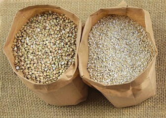 Buckhwheat unroasted and pearl barley, healthy groats in apper bags on jute fabric background