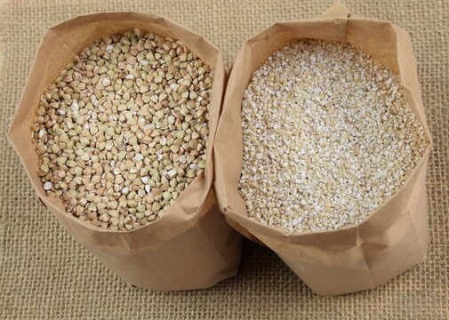 Buckhwheat unroasted and pearl barley, healthy groats in apper bags on jute fabric background