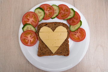 Heart shaped cheese sandwich with vegetables on white plate. Valentine's day breakfast