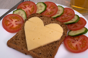 Heart shaped cheese sandwich with vegetables on white plate. Valentine's day breakfast