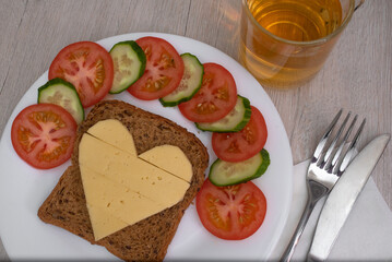 Heart shaped cheese sandwich with vegetables on white plate. Valentine's day breakfast