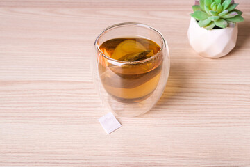 Hot green tea in double walled glass cup with tea bag on table