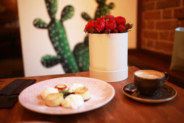 Festive breakfast of a woman on international women's day. On the table are cheesecakes with berries, a cup of coffee and red rose flowers in a round box.