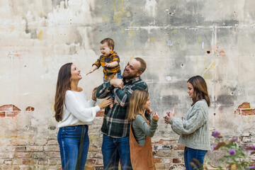 A family of five with two girls and a baby boy standing by an urban old brick wall