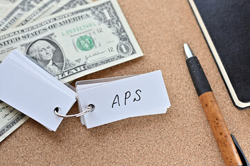 On the desk there are bills, a notebook, and a sticky note with the word APS written on it. It was...