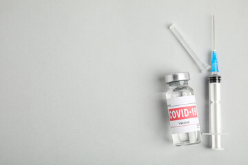 Vial with coronavirus vaccine and syringe on light background, flat lay. Space for text