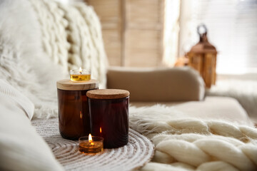 Candles on beige sofa with knitted blanket. Interior design