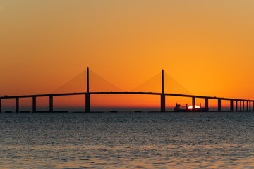 Fototapeta na wymiar Sunrise behind freighter while sailing past bridge