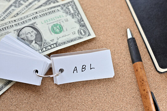 On The Desk There Are Bills, A Notebook, And A Sticky Note With The Word ABL Written On It. It Was An Abbreviation For The Financial Term Asset Based Lending.