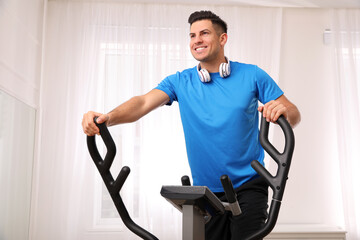 Man with headphones using modern elliptical machine at home