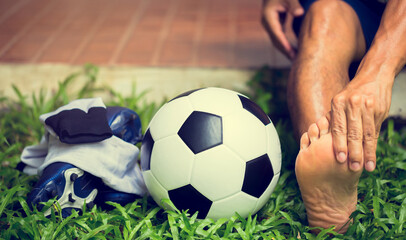 Soccer ball and sport shoes on green grass with soccer player in foot  pain.