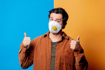 Guy in FFP2 face mask in a good mood on yellow and blue backgrounds