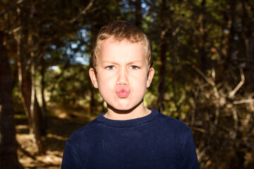 Young boy in a dark forest putting up duck faces to spoil a preadolescent photo