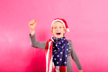 Blond boy with santa hat, American flag and raised fist in victory sign.