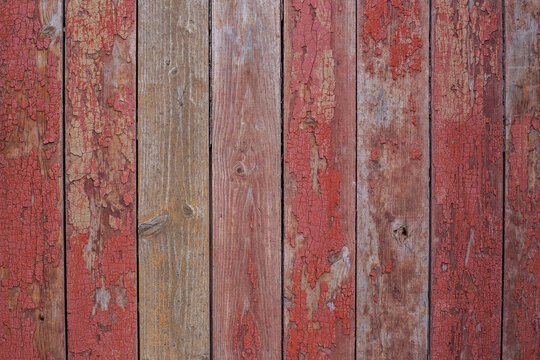Old wooden fence painted in red, peeling cracked paint. Texture of red wooden planks, old barn wall, rustic style © Oksana