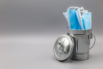Silver garbage bin with lid filled with medical face masks during covid-19 and corona with copy space left