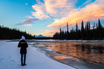 Back view of a woman admiring a colorful sunset sky reflecting in the Athabasca river, in Jasper national park, Canada