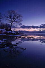 夕暮れの湖の風景。鏡面の湖面に映る黄昏の空と雲。屈斜路湖、北海道、日本。
