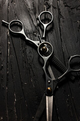 Metallic barber scissors on top of dark background. - obrazy, fototapety, plakaty