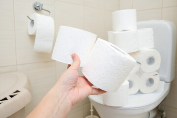 Many toilet paper rolls at home of hoarder, buying too much of hygienic means during pandemia, a hand holding a roll of toilet paper in a bathroom