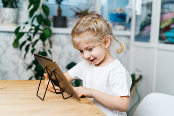 a little girl is sitting at a table with a tablet with her hands raised in the air smiling and happy, experiencing happiness