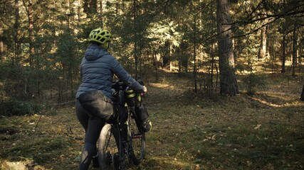 The woman travel on mixed terrain cycle touring with bike bikepacking outdoor. The traveler journey with bicycle bags. Stylish bikepacking, bike, sportswear in green black colors. Magic forest park.