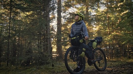 Fototapeta na wymiar The woman travel on mixed terrain cycle touring with bike bikepacking outdoor. The traveler journey with bicycle bags. Stylish bikepacking, bike, sportswear in green black colors. Magic forest park.