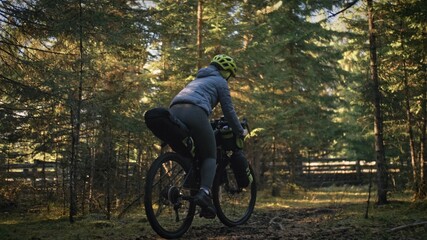 Naklejka premium The woman travel on mixed terrain cycle touring with bike bikepacking outdoor. The traveler journey with bicycle bags. Stylish bikepacking, bike, sportswear in green black colors. Magic forest park.