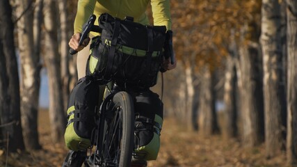 The woman travel on mixed terrain cycle touring with bikepacking. The traveler journey with bicycle bags. Sportswear in green black colors. The trip in magical autumn forest, arch, alley, avenue.