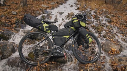 Fototapeta premium The mixed terrain cycle touring bike with bikepacking. The travel journey with light bicycle bags designed or modified for cycling. The trip on bike, outdoor in magical autumn forest, river stream.