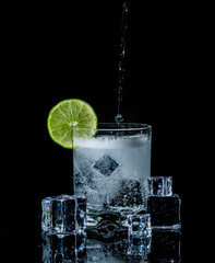 Refreshing drink being poured and splashing  on ice with lime garnish