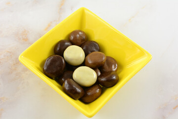 Kruidnoten cookies covered with variety of milk chocolate, dark chocolate and white chocolate in yellow snack bowl on table