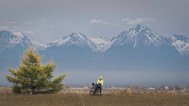 The woman travel on mixed terrain cycle touring with bikepacking. The traveler journey with bicycle bags. Sport tourism bikepacking, bike, sportswear in green black colors. Mountain snow capped.