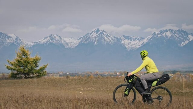 The man and woman travel on mixed terrain cycle touring with bikepacking. The two people journey with bicycle bags. Sport bikepacking, bike, sportswear in green black colors. Mountain snow capped.