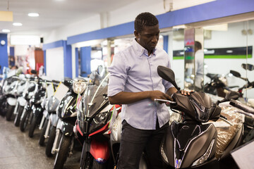 Afro american man is shopping and choosing new motobike in moto store. High quality photo