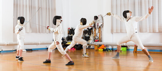 Adults and teens wearing fencing uniform practicing with foil at a gym