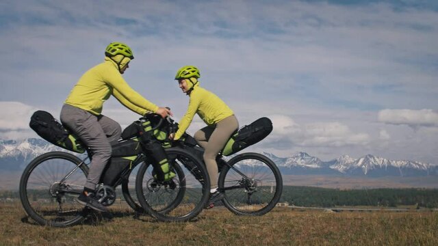 The man and woman travel on mixed terrain cycle touring with bikepacking. The love couple journey with tent in nature with bicycle bags. Stylish bikepacking, bike, sportswear in green black colors.