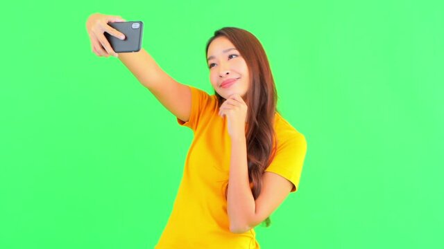 Lively happy Asian woman in yellow t-shirt takes selfies with phone front camera showing V gesture with her fingers