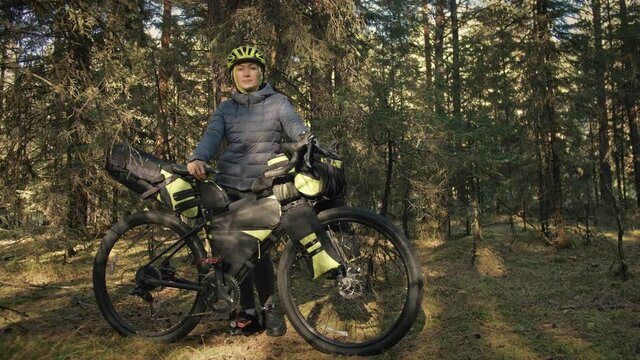 The woman travel on mixed terrain cycle touring with bike bikepacking outdoor. The traveler journey with bicycle bags. Stylish bikepacking, bike, sportswear in green black colors. Magic forest park.