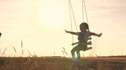 Amusement park dream concept. Happy girl swinging on a swing in the park at sunset. child plays with wooden swing, childhood dream, airplane pilot flights to the sky. A happy family
