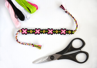 Woven DIY friendship bracelet with abstract pattern near skeins of embroidery floss, scissors