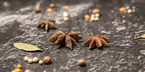 Anise stars Illicium verum, black peppercorns on black stone background. Selective focus, banner