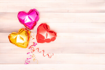 three rose gold and red shiny balloons in the shape of a heart with interlaced ribbons lie on wooden beige and pink boards. Valentine's Day. The 14th of February concept. banner with copyspace. place