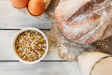 raw different grains and seeds in white porcelain cup, ready-made grain bread, eggs and sourdough. well-being philosophy in food, top view, selective focus