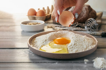raw egg in hand is broken and poured into stylish bowl with flour on background of ingredients for baking at home. selective focus